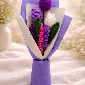 Handmade crochet flower bouquet with tulips and lupine stems wrapped in purple paper on a soft pastel background