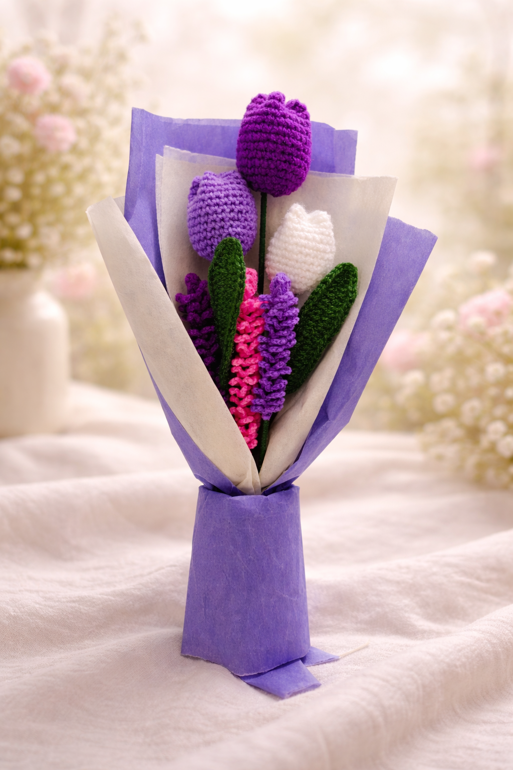 Handmade crochet flower bouquet with tulips and lupine stems wrapped in purple paper on a soft pastel background