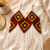 Handmade boho chic crochet halter top featuring colorful granny square motifs with long white fringe, laid flat on a neutral linen background.