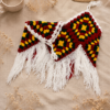 Folded Boho Chic Crochet Halter Top in red, green, yellow and white with long fringe, styled on beige linen with dried flowers and a ceramic mug.