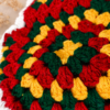 Close-up of the handmade granny square crochet pattern on the Boho Chic Crochet Halter Top, featuring red, green and yellow cotton yarn with intricate textured stitches.