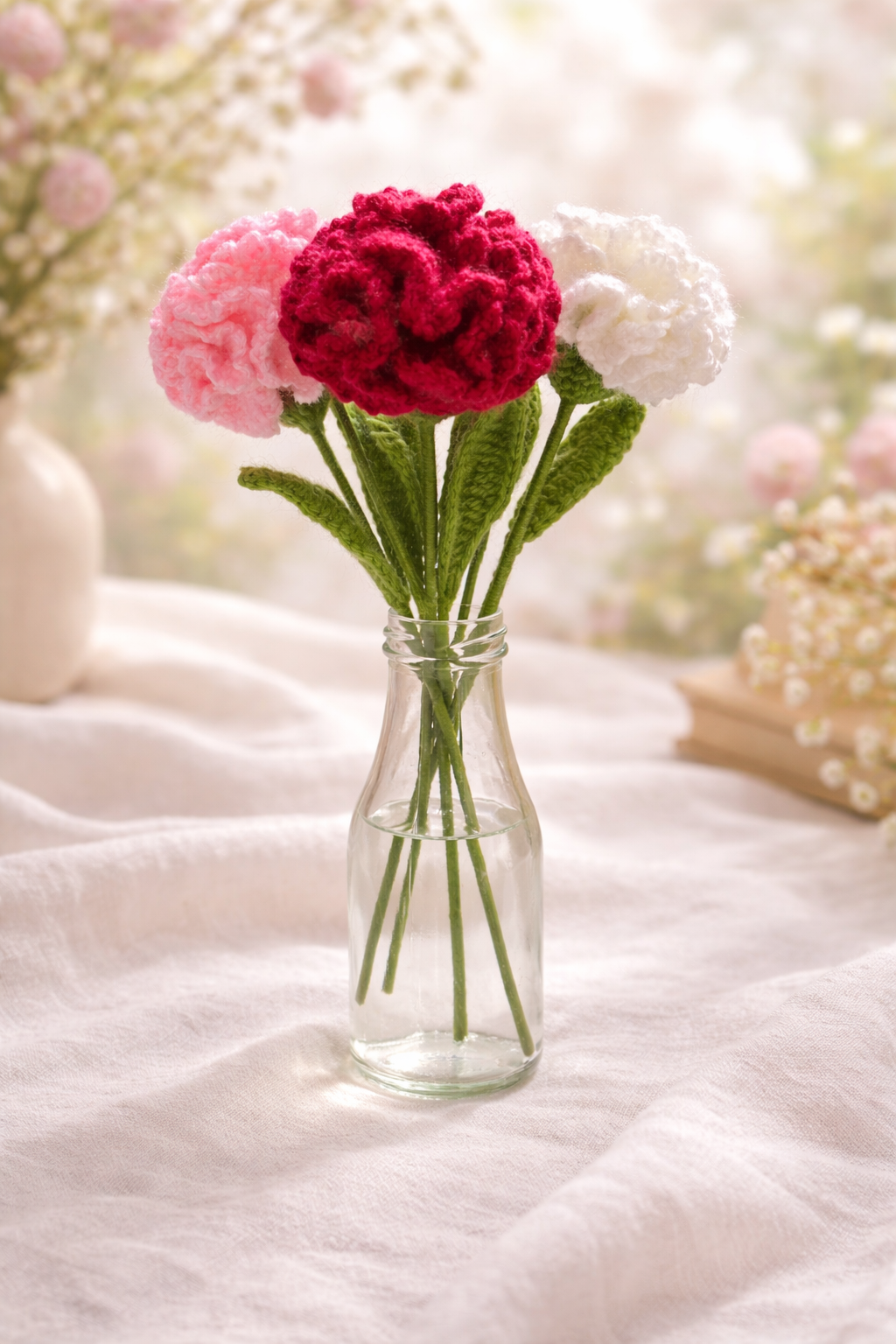 Whispers of Spring – Crochet Carnations (Set of 4)_1 Handmade crochet carnation bouquet in soft pink, red and white tones arranged in a glass vase with a light pastel spring background