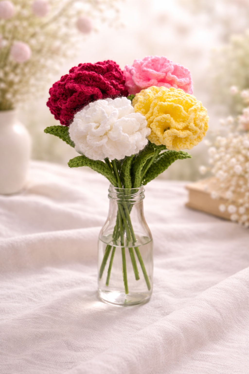 Whispers of Spring – Crochet Carnations (Set of 4)_5 Handmade crochet carnation bouquet set of four in red, pink, white and yellow arranged in a glass vase with soft pastel spring background