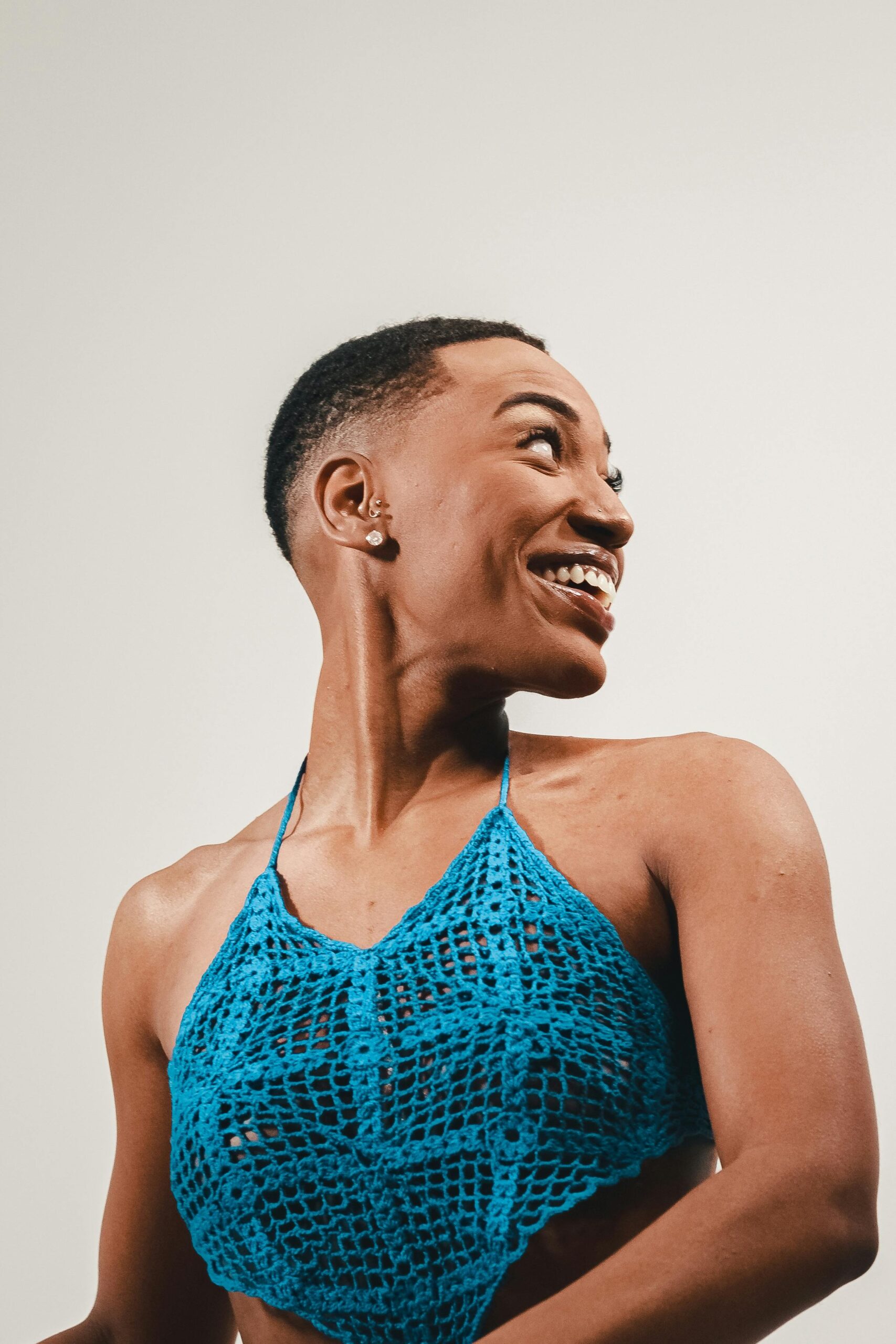 A woman wearing a blue crochet top smiles while looking back in a studio setting with a white background.