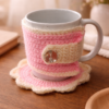 Handmade crochet mug cozy and coaster set in pink and cream on a warm wooden table with soft cozy background