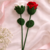 Handmade crochet rose stems in red and white lying on soft pink satin fabric with ribbon and delicate floral accents