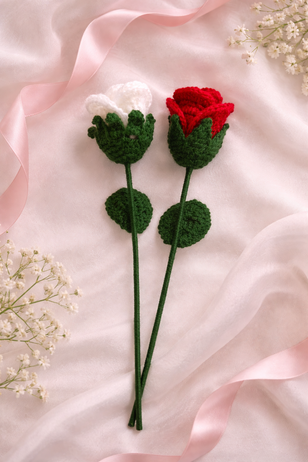 Handmade crochet rose stems in red and white lying on soft pink satin fabric with ribbon and delicate floral accents