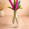 Crochet lupine flower bouquet in glass bottle with pink, orange and blue handmade stems on a warm wooden background
