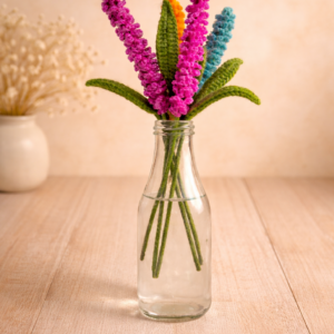 Crochet lupine flower bouquet in glass bottle with pink, orange and blue handmade stems on a warm wooden background