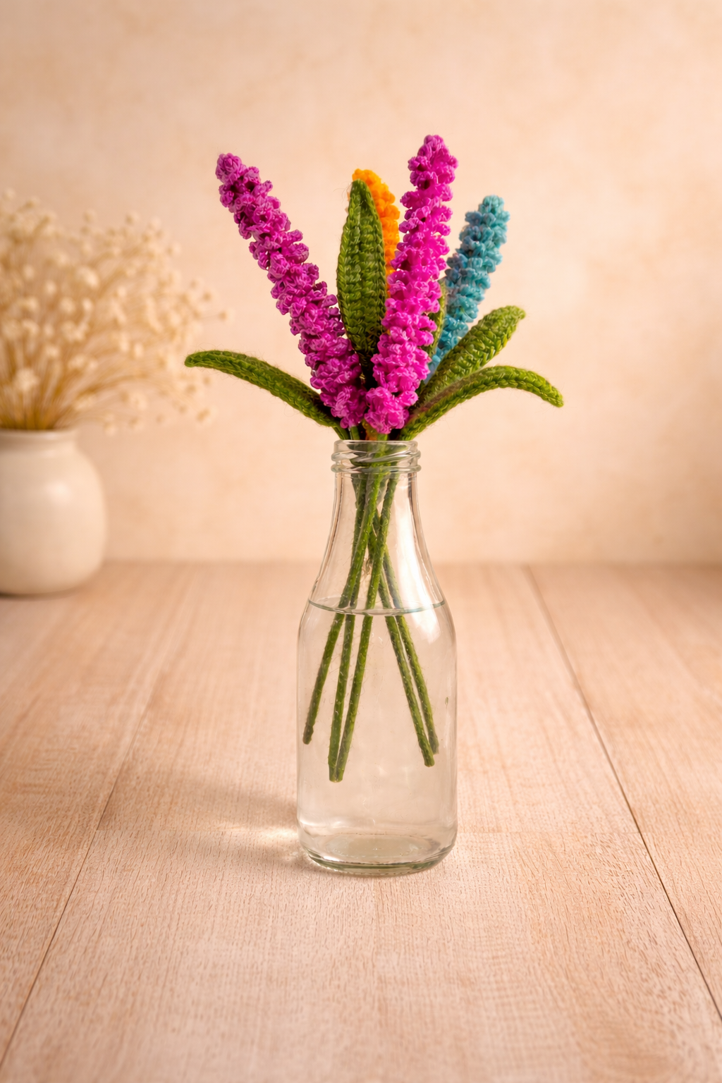 Crochet lupine flower bouquet in glass bottle with pink, orange and blue handmade stems on a warm wooden background