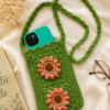 Side Sling Bag_1 Green handmade crochet side sling bag with two floral appliqués, shown with a phone inside on a soft cream fabric background.